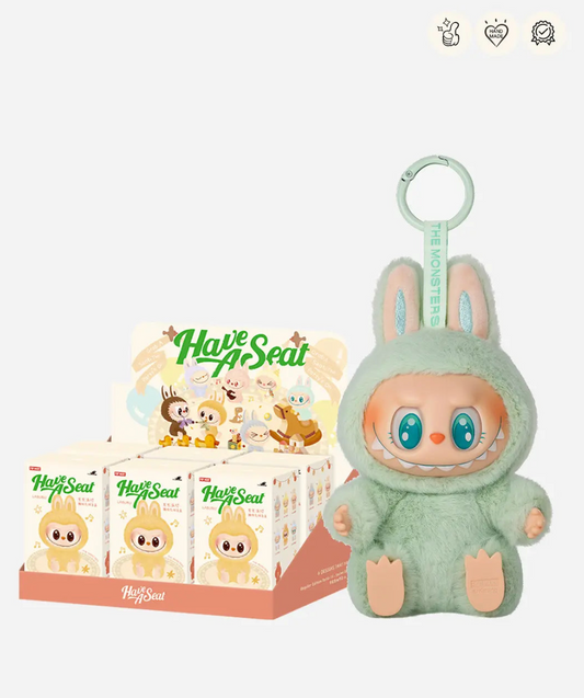 Labubu Have a Seat display case of sealed boxes next to the mint green Ququ figure; small badge icons top right