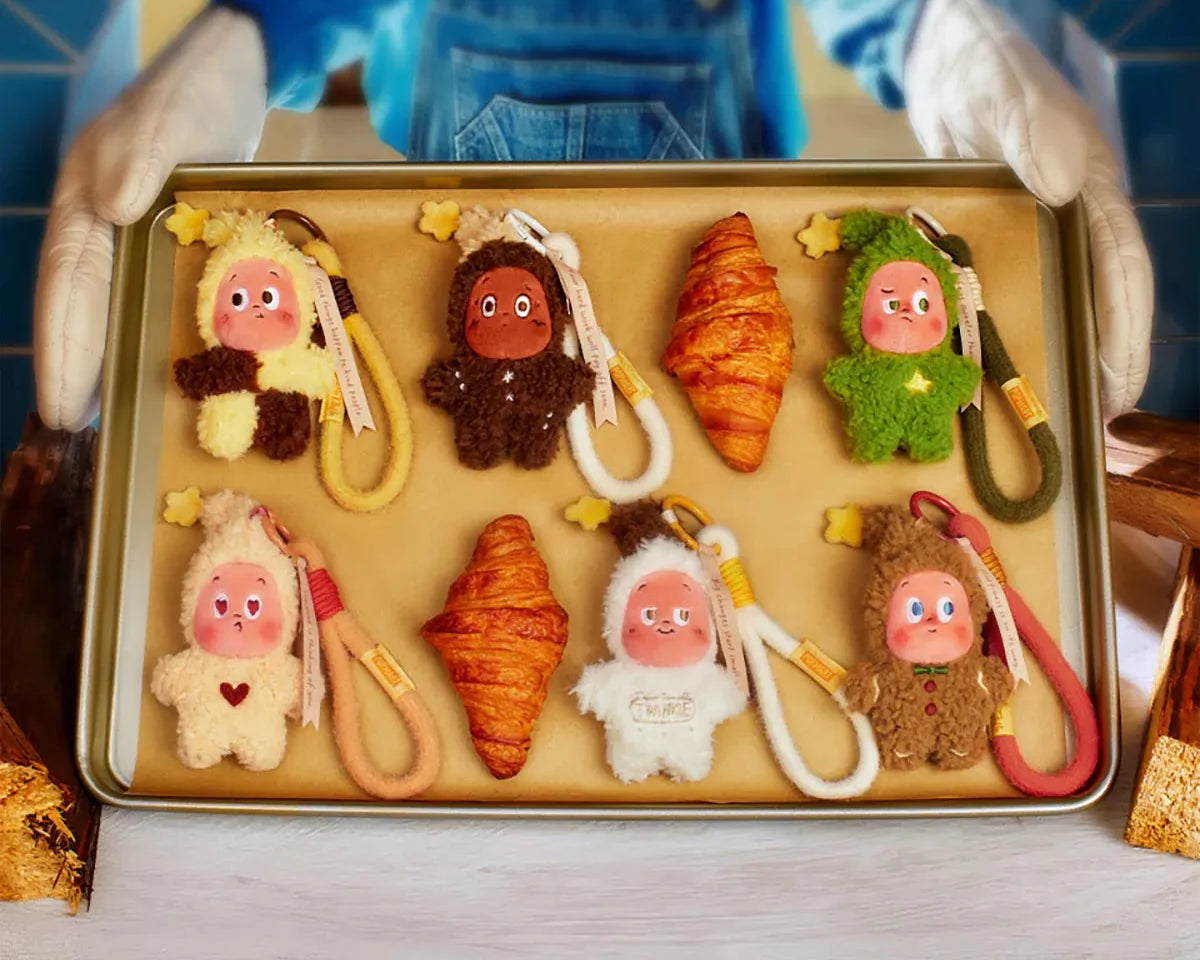 Six Twinkle Twinkle Savor the Moment plush pendants laid out on a baking tray between croissants