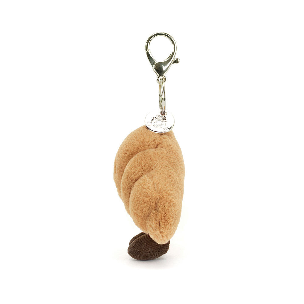 Jellycat Amuseables Croissant plush bag charm from the side, showing the clasp and round metal tag