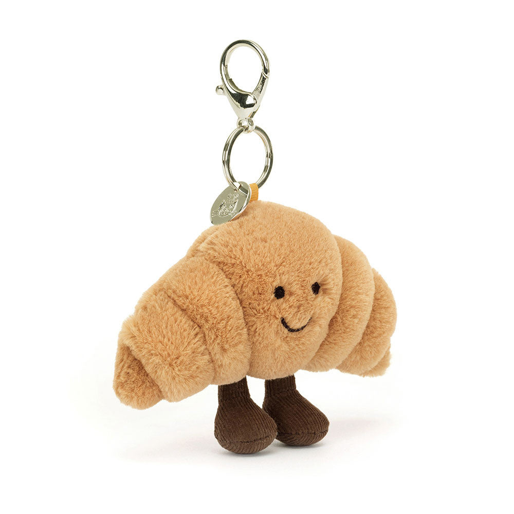 Jellycat Amuseables Croissant plush bag charm, front: smiling golden croissant with brown cord boots and a metal clip