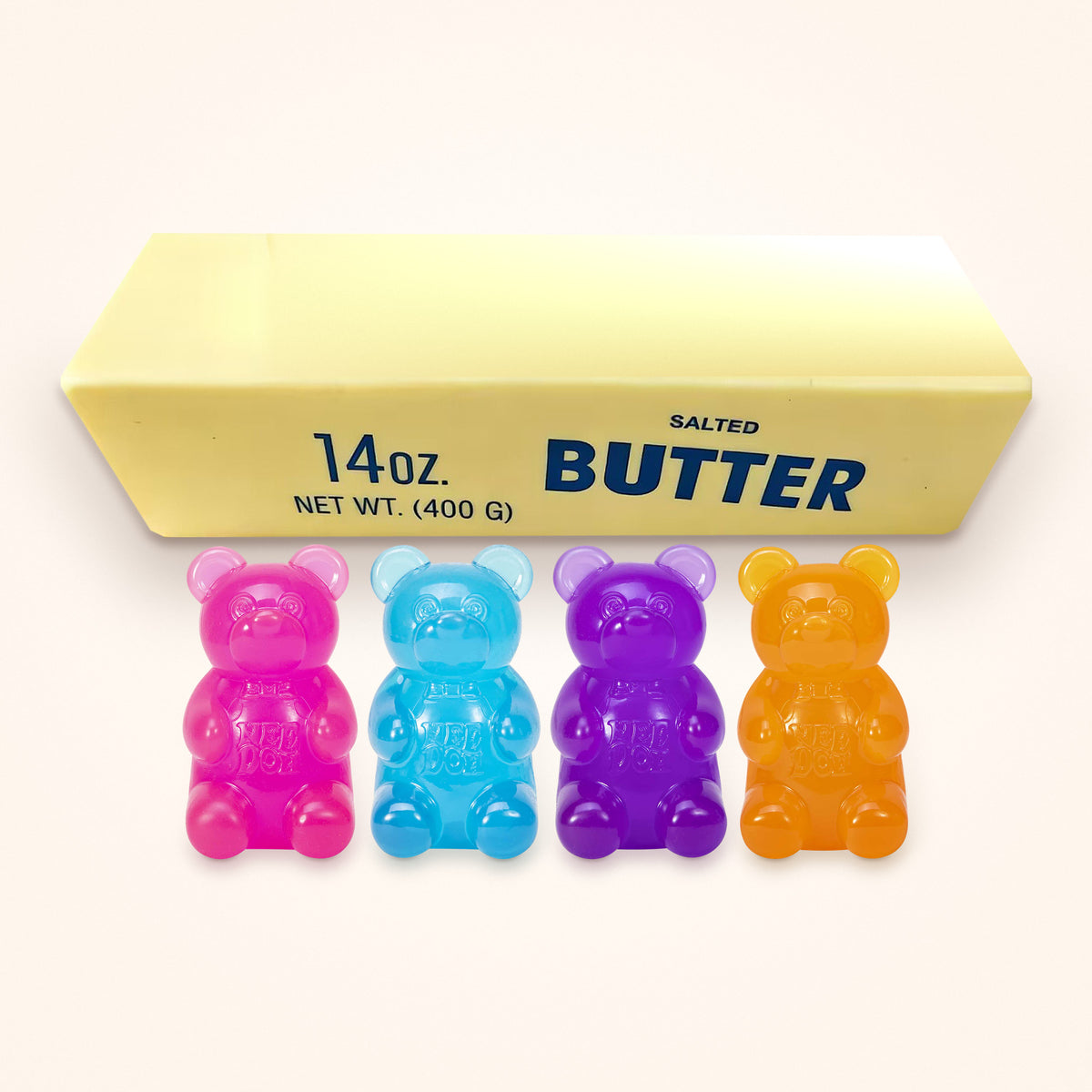 Squishy Gift Box Big Squish: four NeeDoh Gummy Bears in pink, blue, purple and orange in front of a Giant Butter Squishy, shown to scale on a cream background