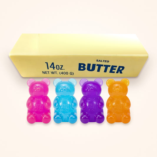 Squishy Gift Box Big Squish: four NeeDoh Gummy Bears in pink, blue, purple and orange in front of a Giant Butter Squishy, shown to scale on a cream background