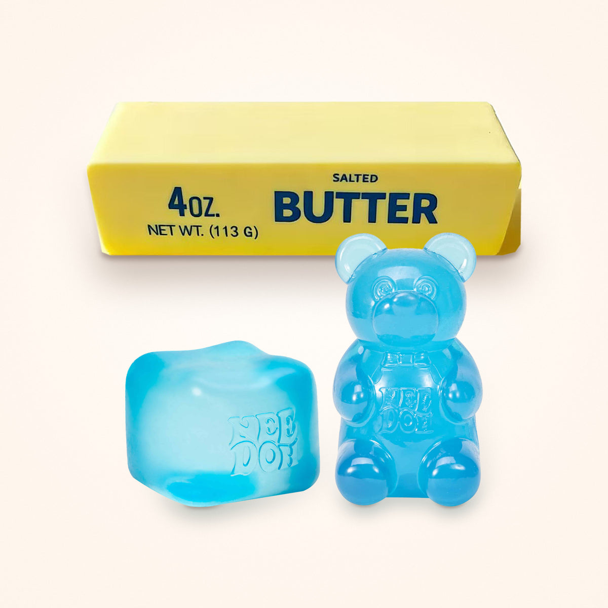 Squishy Gift Box Trio: a blue NeeDoh Nice Cube and a blue NeeDoh Gummy Bear in front of a Mini Butter Squishy, shown to scale on a cream background