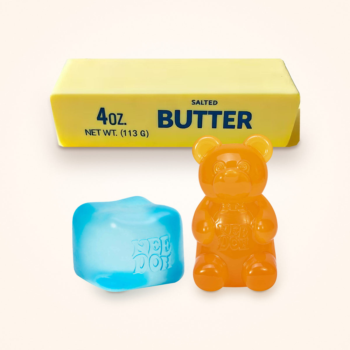 Squishy Gift Box Trio: a blue NeeDoh Nice Cube and a orange NeeDoh Gummy Bear in front of a Mini Butter Squishy, shown to scale on a cream background