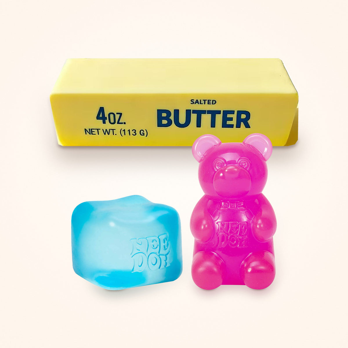 Squishy Gift Box Trio: a blue NeeDoh Nice Cube and a pink NeeDoh Gummy Bear in front of a Mini Butter Squishy, shown to scale on a cream background