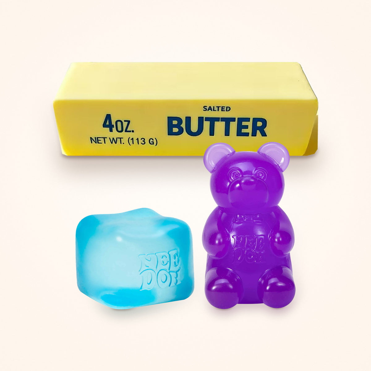 Squishy Gift Box Trio: a blue NeeDoh Nice Cube and a purple NeeDoh Gummy Bear in front of a Mini Butter Squishy, shown to scale on a cream background