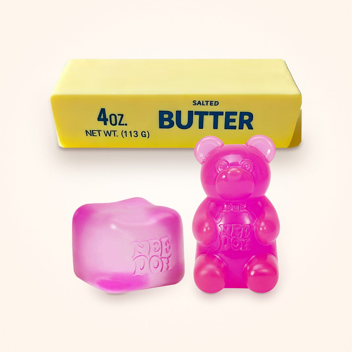 Squishy Gift Box Trio: a pink NeeDoh Nice Cube and a pink NeeDoh Gummy Bear in front of a Mini Butter Squishy, shown to scale on a cream background