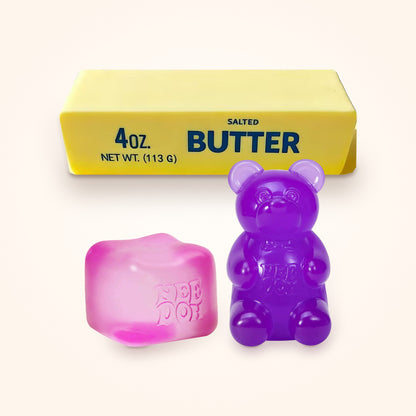 Squishy Gift Box Trio: a pink NeeDoh Nice Cube and a purple NeeDoh Gummy Bear in front of a Mini Butter Squishy, shown to scale on a cream background