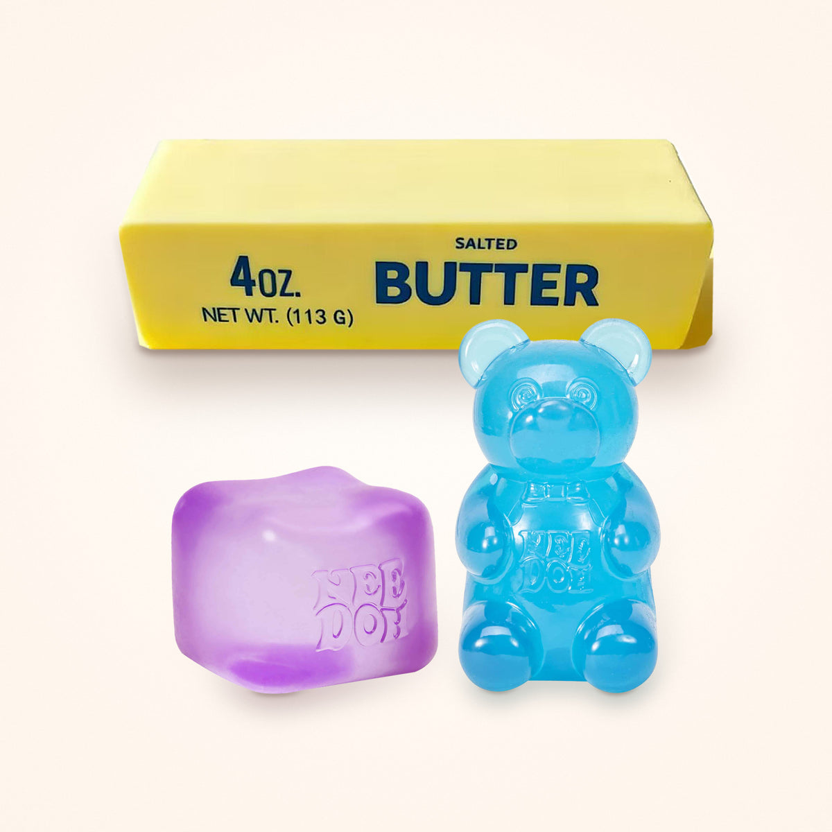 Squishy Gift Box Trio: a purple NeeDoh Nice Cube and a blue NeeDoh Gummy Bear in front of a Mini Butter Squishy, shown to scale on a cream background