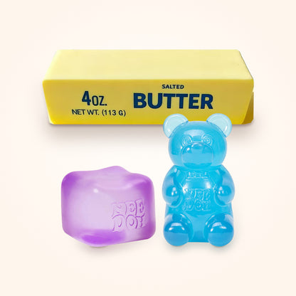 Squishy Gift Box Trio: a purple NeeDoh Nice Cube and a blue NeeDoh Gummy Bear in front of a Mini Butter Squishy, shown to scale on a cream background