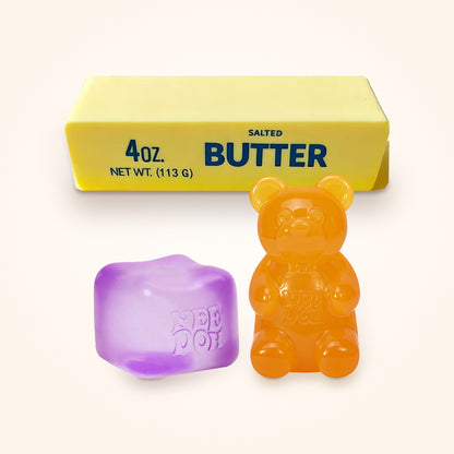 Squishy Gift Box Trio: a purple NeeDoh Nice Cube and a orange NeeDoh Gummy Bear in front of a Mini Butter Squishy, shown to scale on a cream background