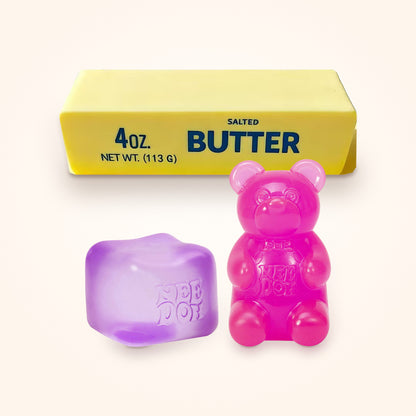Squishy Gift Box Trio: a purple NeeDoh Nice Cube and a pink NeeDoh Gummy Bear in front of a Mini Butter Squishy, shown to scale on a cream background